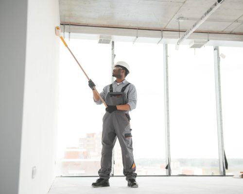 African man paints a white wall with a roller. Repair of the interior.